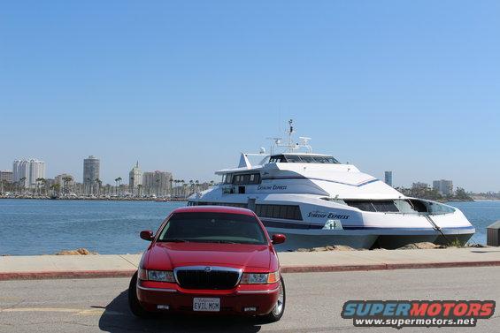 Red 2002 Mercury Grand Marquis parked in front of a large white passenger ferry and a city skyline