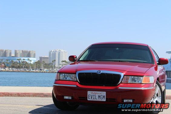 Red 2002 Mercury Grand Marquis parked by the water with city buildings in the background