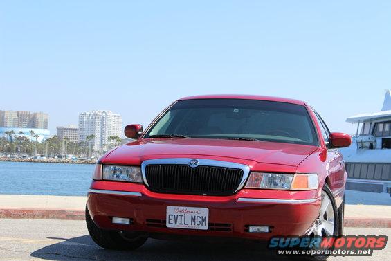 Red 2002 Mercury Grand Marquis with custom 'EVIL MGM' license plate, front view, parked by a waterfront