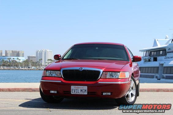 Red 2002 Mercury Grand Marquis parked by the water with a boat in the background