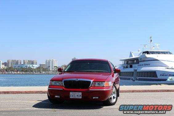 Red 2002 Mercury Grand Marquis parked by a large white boat and city skyline