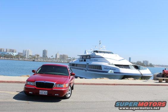 Red 2002 Mercury Grand Marquis parked by a harbor with a large white passenger ferry behind it
