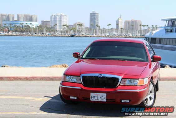 Red 2002 Mercury Grand Marquis with California plate 'EVIL MGM' parked near a harbor