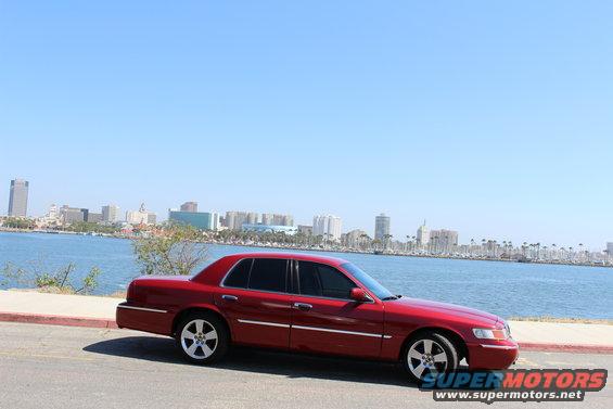 Red 2002 Mercury Grand Marquis parked by the water with a city skyline in the background