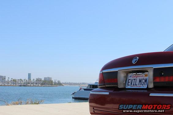 Red 2002 Mercury Grand Marquis parked by the water with boats and a city skyline in the background
