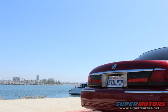 Red 2002 Mercury Grand Marquis rear view with license plate EVIL MGM parked by a waterfront