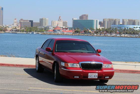 2002 Mercury Grand Marquis parked by the water, city skyline behind it. License plate reads EVIL MGM