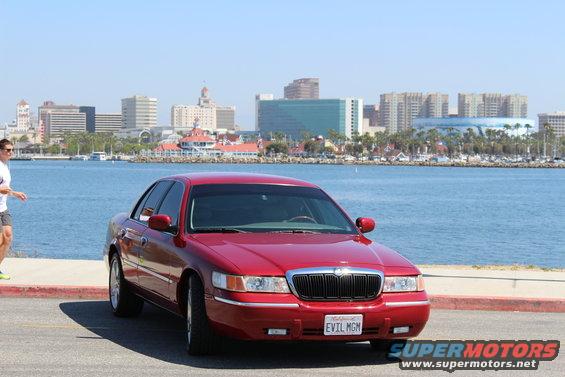 Red 2002 Mercury Grand Marquis parked by the water with a city skyline in the background
