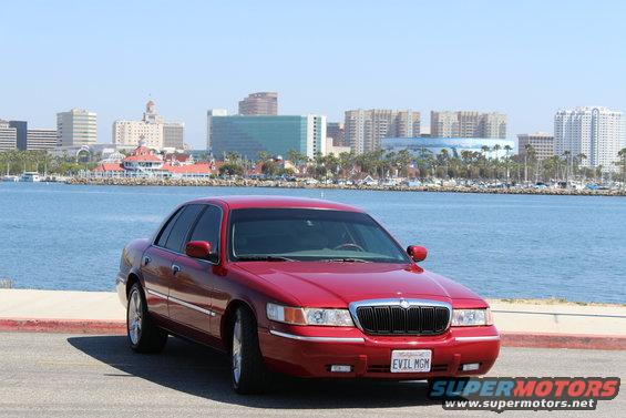 Red 2002 Mercury Grand Marquis parked by the water with a city skyline in the background