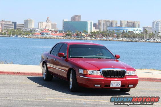 Red 2002 Mercury Grand Marquis parked by the water with a city skyline in the background