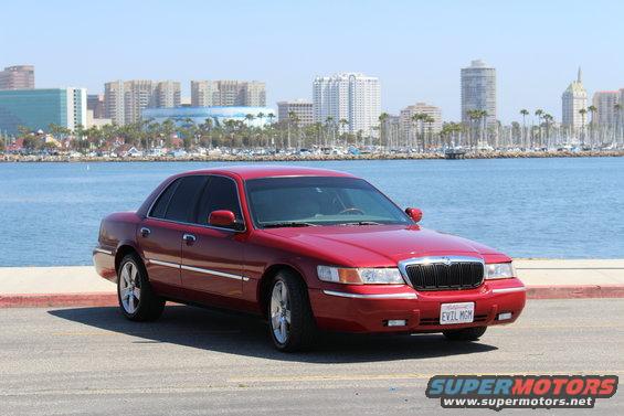 Red 2002 Mercury Grand Marquis parked by the water with city buildings in the background