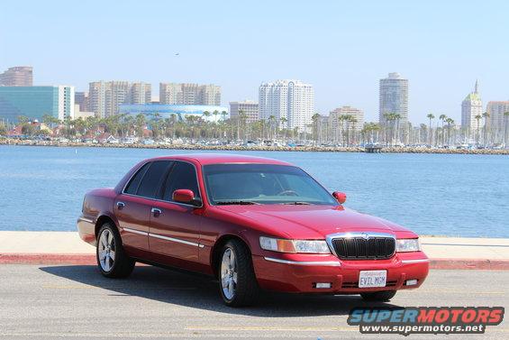 Red 2002 Mercury Grand Marquis parked by the water with a city skyline in the background