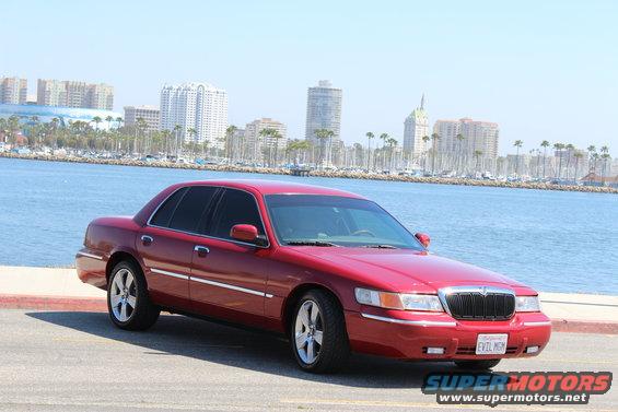 Red 2002 Mercury Grand Marquis parked by the water with city buildings in the background