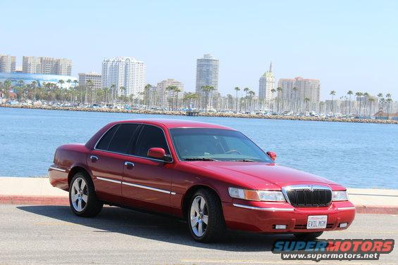 2002 Mercury Grand Marquis parked by the water with city skyline in background. License plate reads EVIL MGM