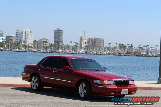 Red 2002 Mercury Grand Marquis parked by the water with city buildings in the background
