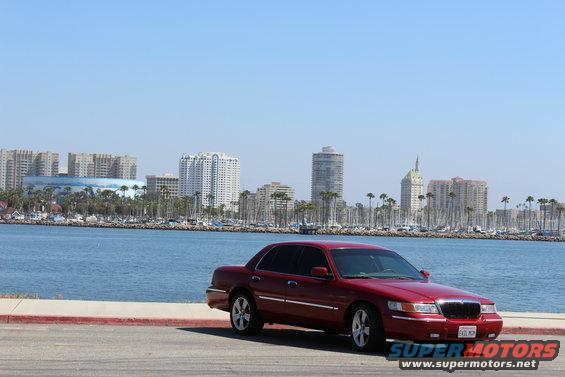 Red 2002 Mercury Grand Marquis parked by the water with a city skyline in the background