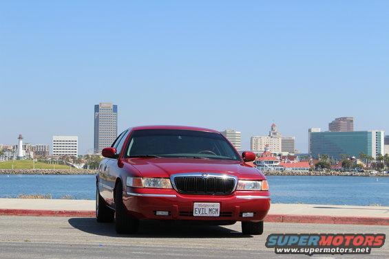 Red 2002 Mercury Grand Marquis parked by the water with a city skyline in the background