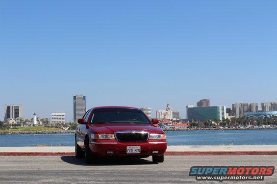 Red 2002 Mercury Grand Marquis parked by the water, front view, with a city skyline in the background