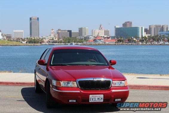 Red 2002 Mercury Grand Marquis parked by the water with a city skyline in the background