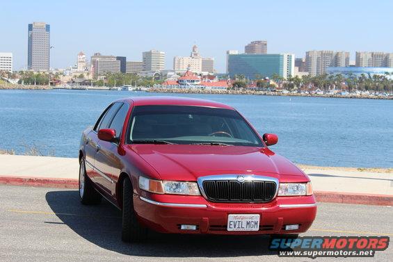 Red 2002 Mercury Grand Marquis parked by the water with a city skyline in the background