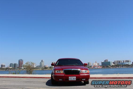 Red 2002 Mercury Grand Marquis parked by the water with a city skyline