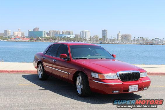 Red 2002 Mercury Grand Marquis parked by the water with a city skyline in the background