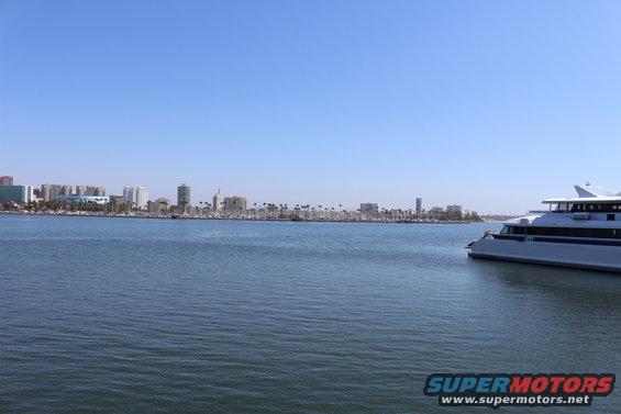 Large white passenger ferry boat sailing on blue water with city skyline in background
