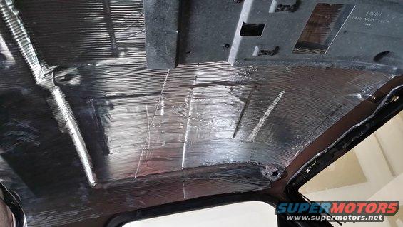 Vehicle interior ceiling covered in silver soundproofing material, showing exposed metal and wiring