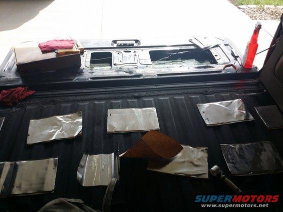 Soundproofing sheets laid out in the bed of a pickup truck, with tools and a bottle nearby