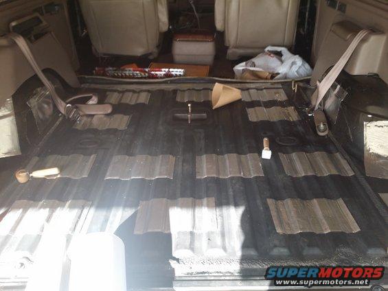 Vehicle interior showing corrugated floor with soundproofing material and two front seats