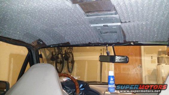 interior of a vehicle with soundproofing material on the headliner, two bikes hanging from the ceiling, and a spray can on the dash