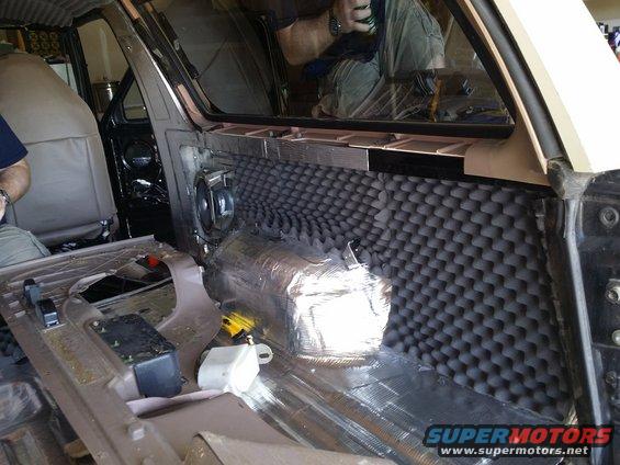 Interior of a vehicle with soundproofing foam on the door panel and insulation on the floor. A speaker is visible in the door