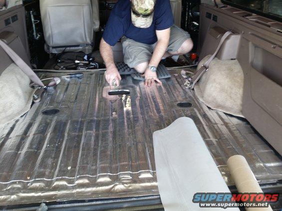 Interior of a vehicle with corrugated metal floor being covered with soundproofing material by a man