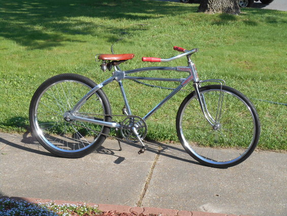 Chrome bicycle with red handlebars and seat, parked on a sidewalk