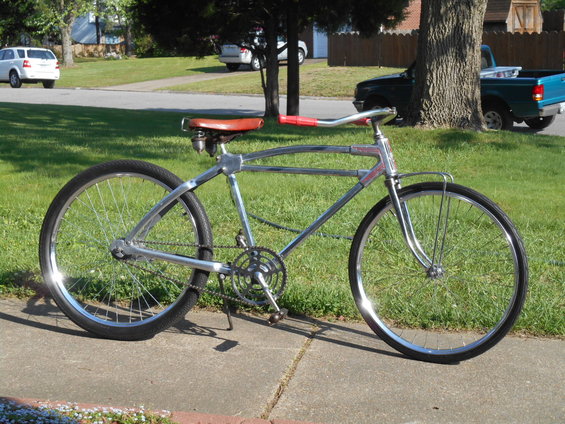 Chrome bicycle with red handlebars and brown seat, parked on a sidewalk