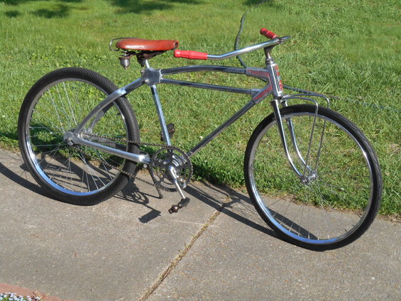 Chrome bicycle with red handlebars and seat, parked on a sidewalk