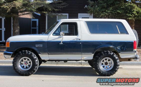 Two-tone blue and white Ford Bronco with off-road tires parked on a street
