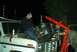 1979 Ford Bronco - Mechanics work on removing an engine from a white truck using a red engine hoist at night.