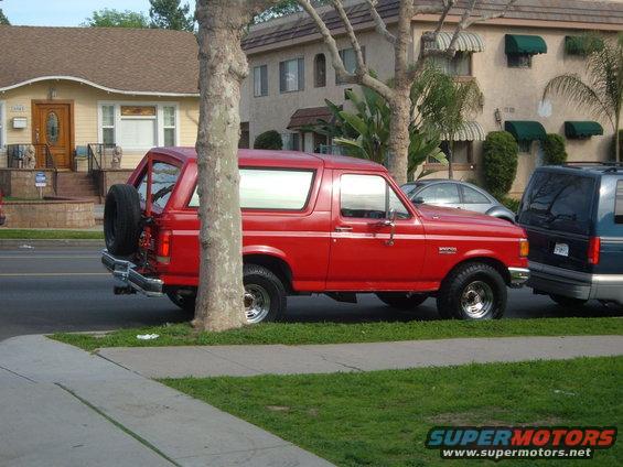 Red 1988 Ford Bronco parked on street next to a dark blue van