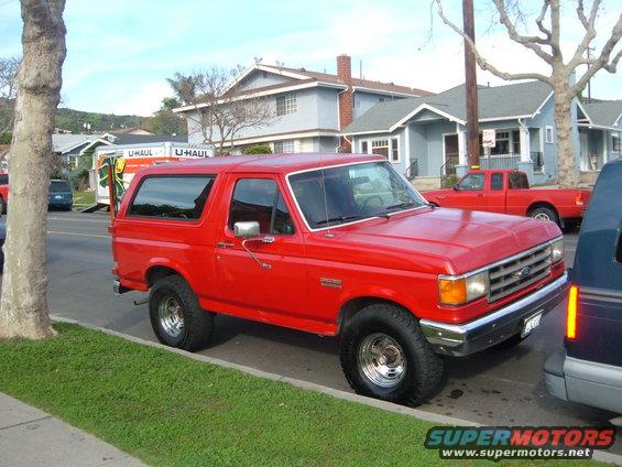 Red 1988 Ford Bronco parked on street, U-Haul truck and red pickup in background