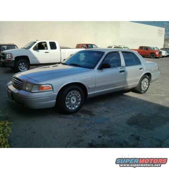 Silver 2004 Ford Crown Victoria sedan, 3/4 front view. Multiple trucks in background