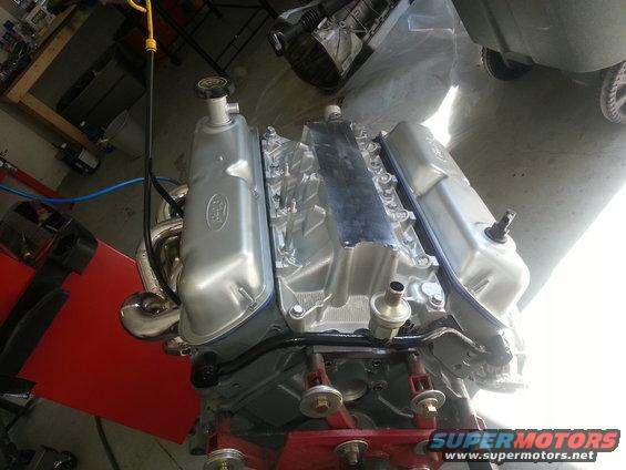 Silver Ford V8 engine on a red stand, with chrome exhaust headers and a yellow dipstick