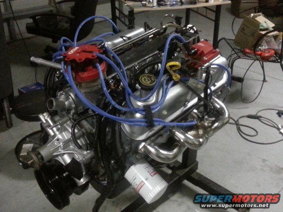 V8 engine with red distributor cap and blue spark plug wires, sitting on an engine stand