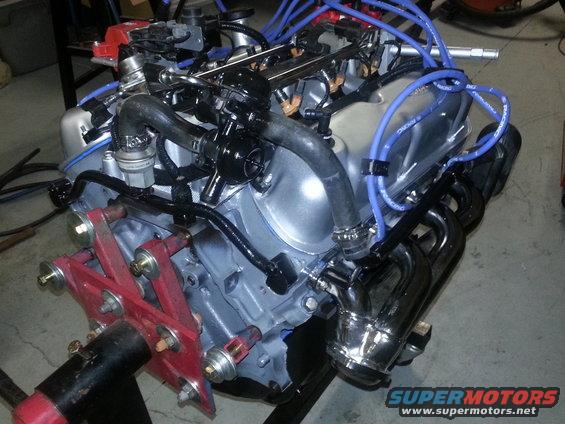 Engine with blue spark plug wires and chrome headers on a stand