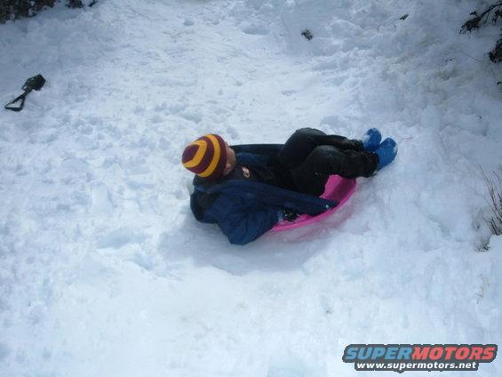 Person wearing a striped hat and blue boots lies on a pink sled in the snow