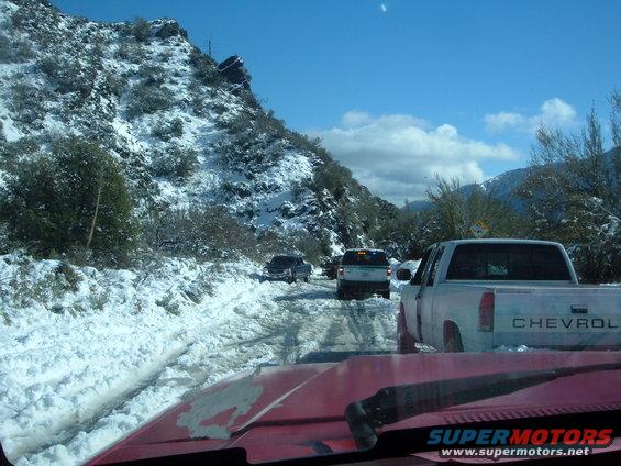 Traffic jam on a snowy mountain road with several trucks and SUVs. View from inside a red vehicle