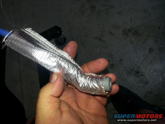 Hand holding a blue hose wrapped in silver heat-shielding material with a gray connector