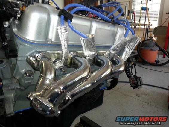Chrome exhaust manifold attached to a silver engine with blue spark plug wires