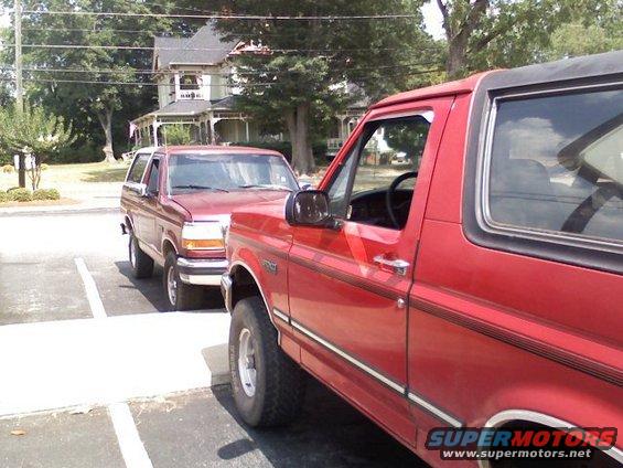 Two red Ford Broncos parked, one in foreground, one behind. Visible grille and body style match 1992