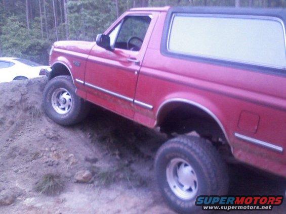 Red 1992 Ford Bronco climbing a dirt hill with a white car in the background